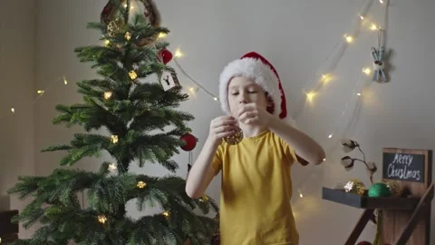Boy decorates a Christmas tree by hanging Christmas toy balls in the room Stock Footage 291609170