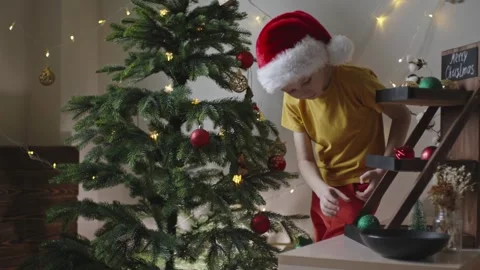 Boy decorates a Christmas tree by hanging Christmas toy balls in the room Stock Footage 291609269