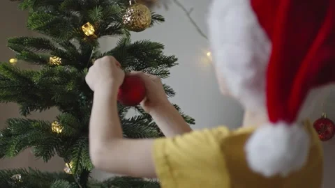 Boy decorates a Christmas tree by hanging Christmas toy balls in the room Stock Footage 291609368