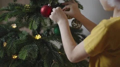 Boy decorates a Christmas tree by hanging Christmas toy balls in the room Stock Footage 291609784
