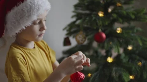 Boy decorates a Christmas tree by hanging Christmas toy balls in the room Stock Footage 291609810