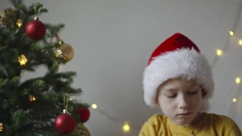 Boy decorates a Christmas tree by hanging Christmas toy balls in the room Stock Footage 291609975