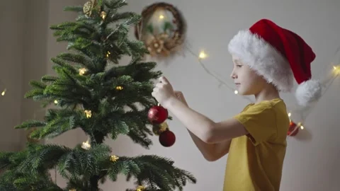Boy decorates a Christmas tree by hanging Christmas toy balls in the room Stock Footage 291610208
