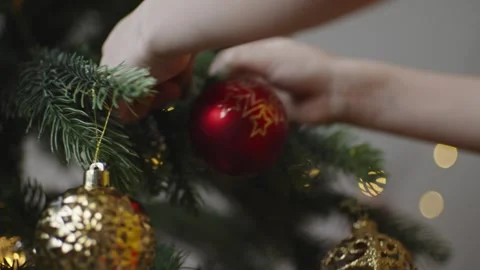 Boy decorates a Christmas tree by hanging Christmas toy balls in the room Stock Footage 291610641