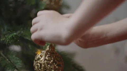 Boy decorates a Christmas tree by hanging Christmas toy balls in the room Stock Footage 291610856