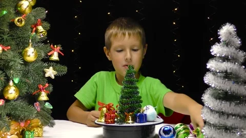 A boy decorates a rotating surface near a small Christmas tree Stock Footage 253312379