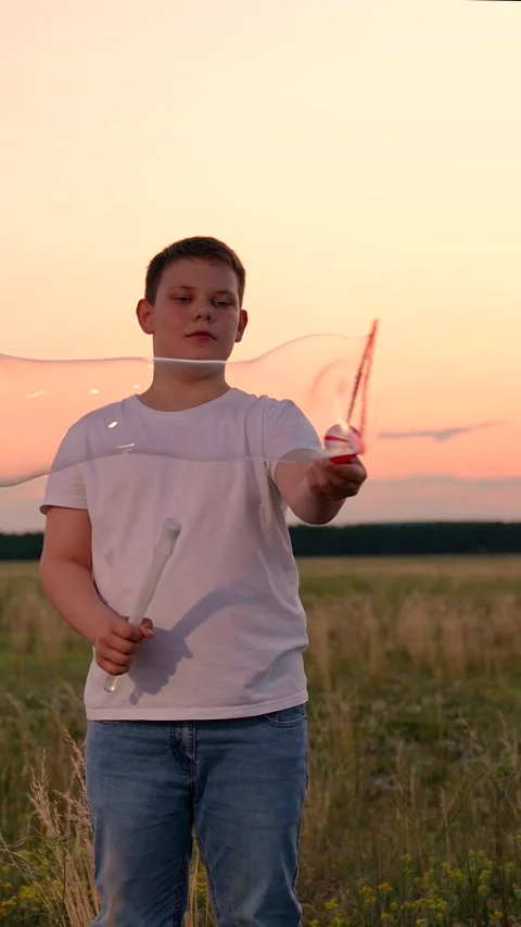 Boy delighted with blowing big soap bubbles. Slow motion. Teenage boy playing Stock Footage 313161004