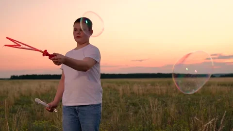 Boy delighted with blowing big soap bubbles. Slow motion. Teenage boy playing Stock Footage 314345710