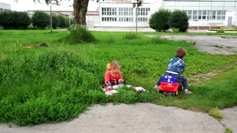 A boy in a denim jacket sits on a toy car, a girl roller-skates, happy children, Vídeo Stock 271202437