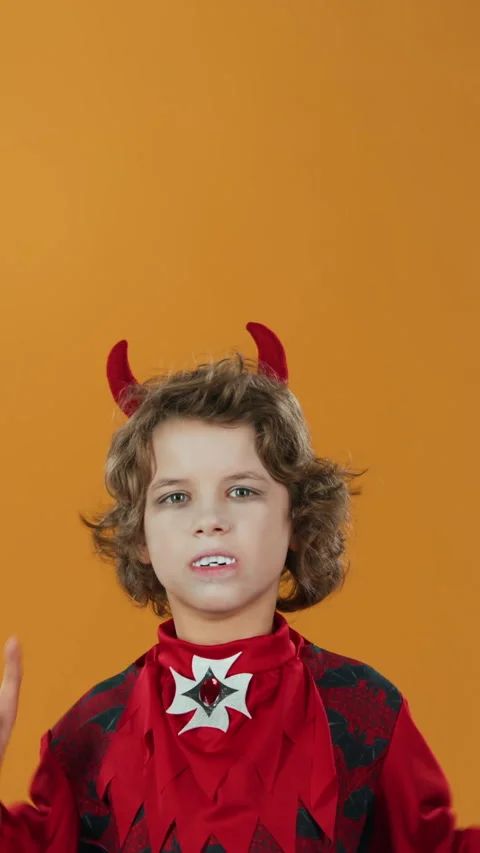 Boy in Devil Costume, with Fangs and Horns Pointing Upward on Orange Backdrop Stock Footage 285842724