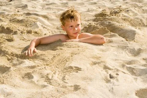 Boy is digging oneself into the sandy beach and has a lot of fun Stock Photos