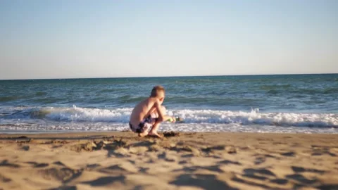 A boy digs sand on the beach with a plastic scoop or shovel. Stock Footage 205366994