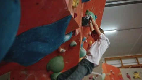 The boy diligently climbs the artificial rocks of the climbing wall Stock Footage 276334290