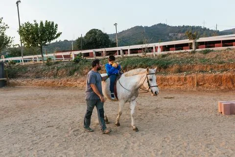 Boy with a disability doing exercises during an equine therapy session. Stock Photos