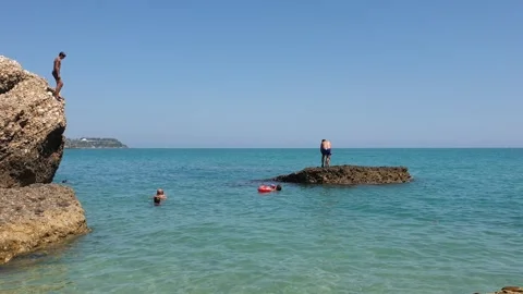 Boy diving from a rock into the ocean on a sunny holiday Stockbeeldmateriaal 280792906