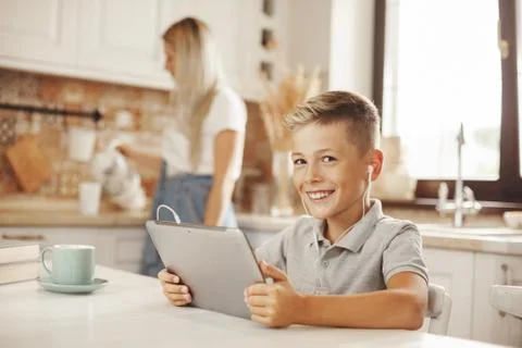 The boy does his homework in the kitchen on the tablet online, talking with the Foto stock