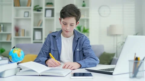 The boy does his homework using a laptop computer writes in notebook sitting at  Stock Footage 238632013