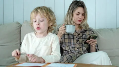 The boy does his homework while his mother drinks tea and uses the phone Video stock 296447543