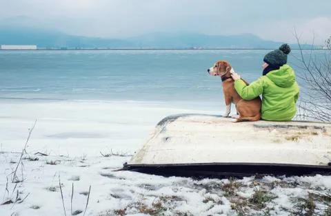 Boy with dog sitting together on the old boat near winter lake Foto stock