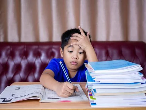 Boy doing homework and reading on a wooden table with a pile of books beside  Stock Photos