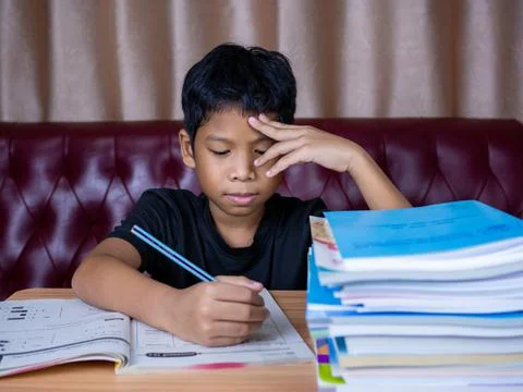 Boy doing homework and reading on a wooden table with a pile of books beside  Stock Photos