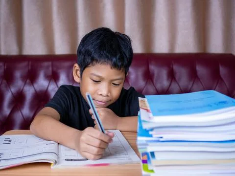 Boy doing homework and reading on a wooden table with a pile of books beside  Stock Photos