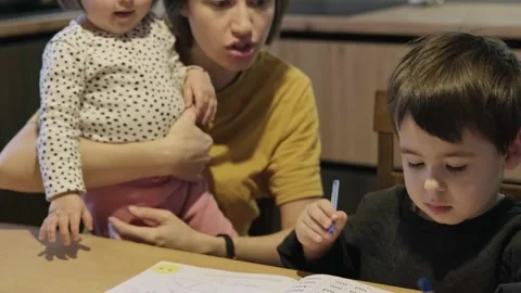 Boy doing homework at home with school books helped by his mother. Mum teaching Stock Footage 172506324