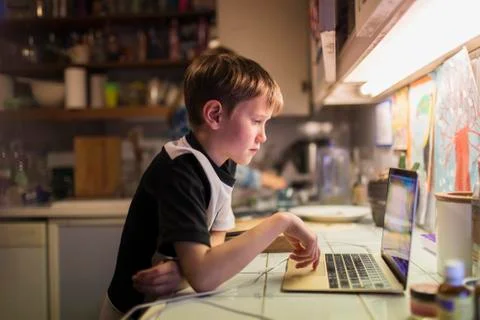 Boy doing homework at laptop on kitchen counter Stock Photos