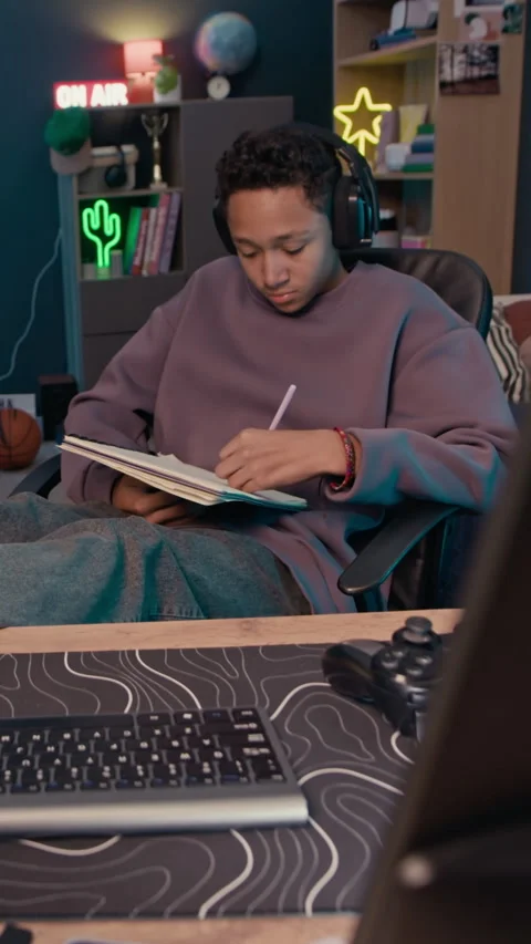 Boy Doing Homework in Relaxed Pose at Home Table with Video Gaming Equipment Stock Footage 319730643
