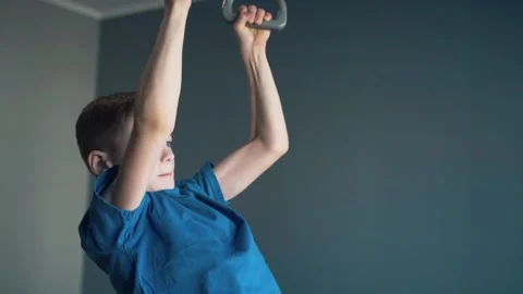 Boy doing pull-ups in a gym on gymnastic rings at home Stock Footage 87352340