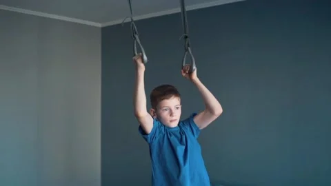 Boy doing pull-ups in a gym on gymnastic rings at home 스톡 동영상 87352342