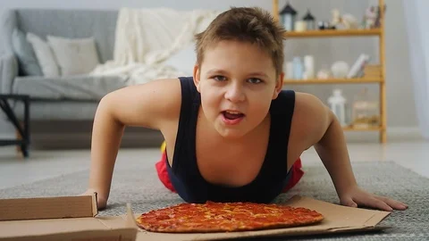 Boy doing push-UPS from the floor where the pizza is Stock Footage 100146315