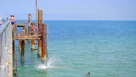 Boy doing a somersault off a pier into the ocean Stock Footage 125061954