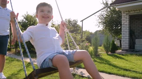 A boy with Down syndrome having fun on a swing with his father. Stock Footage 165042650
