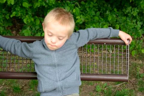 Boy with down syndrome resting on the bench in a park. Stock Photos