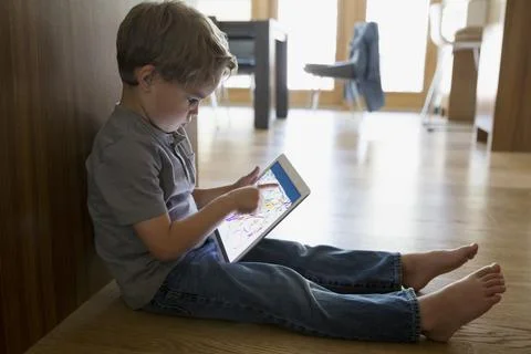 Boy drawing with digital tablet on kitchen hardwood floor Stock Photos
