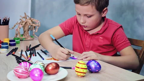 A boy is drawing an Easter drawing with coloured pencils on a sheet of paper Stock Footage 172330419
