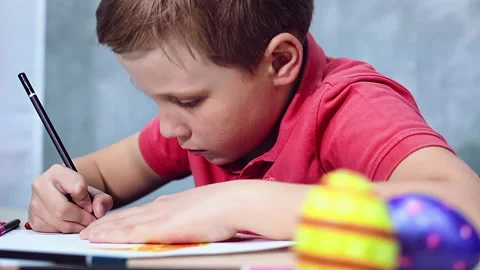 A boy is drawing an Easter drawing with pencils on a sheet of paper Stock Footage 172329353