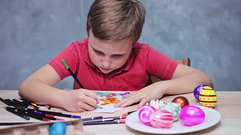 A boy is drawing an Easter drawing with pencils on a sheet of paper Stock Footage 172330551