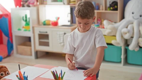Boy drawing with red pencil and visible hand on paper at a bright playroom .. Stock Footage 337372798
