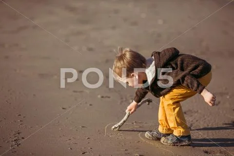 A boy is drawing on the sand with a stick Stock Photos