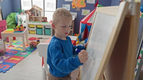 Boy drawing on whiteboard holding marker in a colorful playroom inside a bu.. Stock Footage 339257372