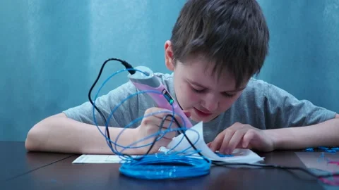 The boy draws with a 3D pen. he raises his face and smiles at the camera Stock Footage 146652049