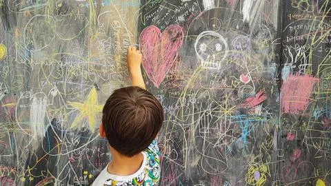 A boy draws with colored chalks on a board with drawings. A large board with  Foto stock
