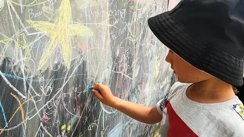 A boy draws with colored chalks on a board with drawings. A large board with  Stock Photos