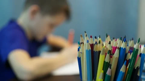 A boy draws a drawing on paper. boy in out of focus, pencils in the foreground Stock Footage 145276328