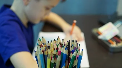 The boy draws a drawing on paper with colored pencils. boy in out of focus Stock Footage 145145119