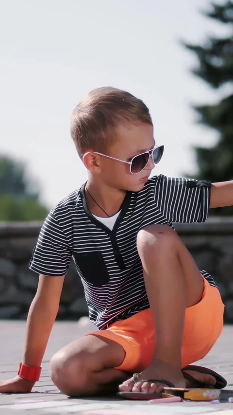 A boy draws drawings with colored crayons on the asphalt, street tiles. A hot Stock Footage 309448143