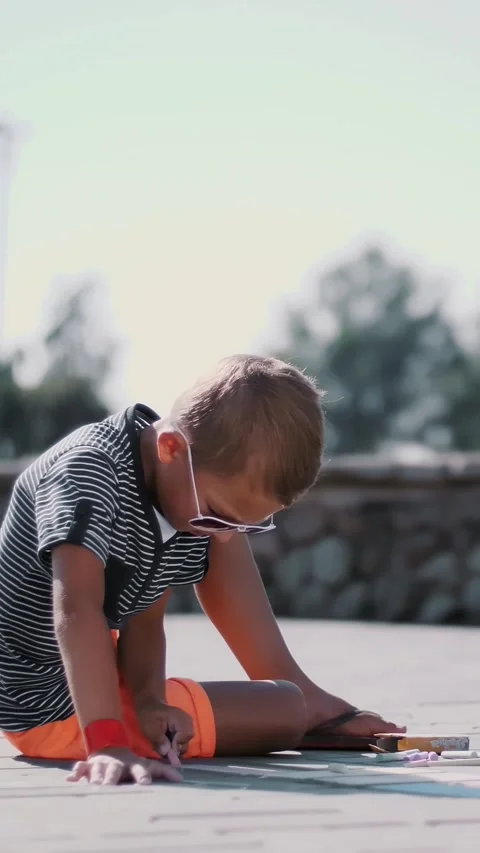 A boy draws drawings with colored crayons on the asphalt, street tiles. A hot Stock Footage 314886747