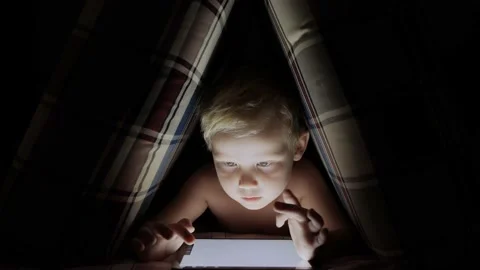 A boy draws on an electronic tablet in a pillow hut in the dark Stock Footage 220802632